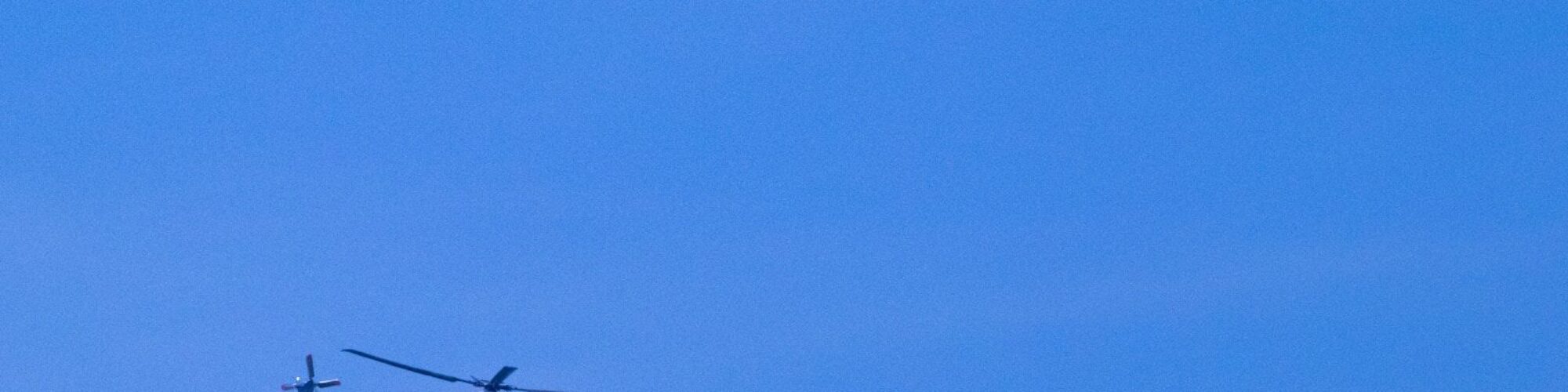 a helicopter flying through a blue sky with no clouds